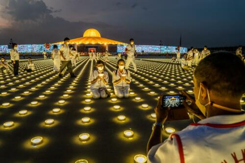 A grounds staff takes a photo of devotees as they light LED lanterns and pray together as a part of the Earth Day 2022 celebration at Wat Phra Dhammakaya Temple. Photographer: Matt Hunt / Neato